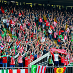 Stadium Crowd**

"A vibrant, cheering crowd at a Ekstraklasa football match in a modern stadium, supporters wearing team jerseys and holding up scarves, fully clothed, appropriate content, safe for work, professional photography, dynamic composition, bright colors, showcasing positive sportsmanship, modest attire."

**